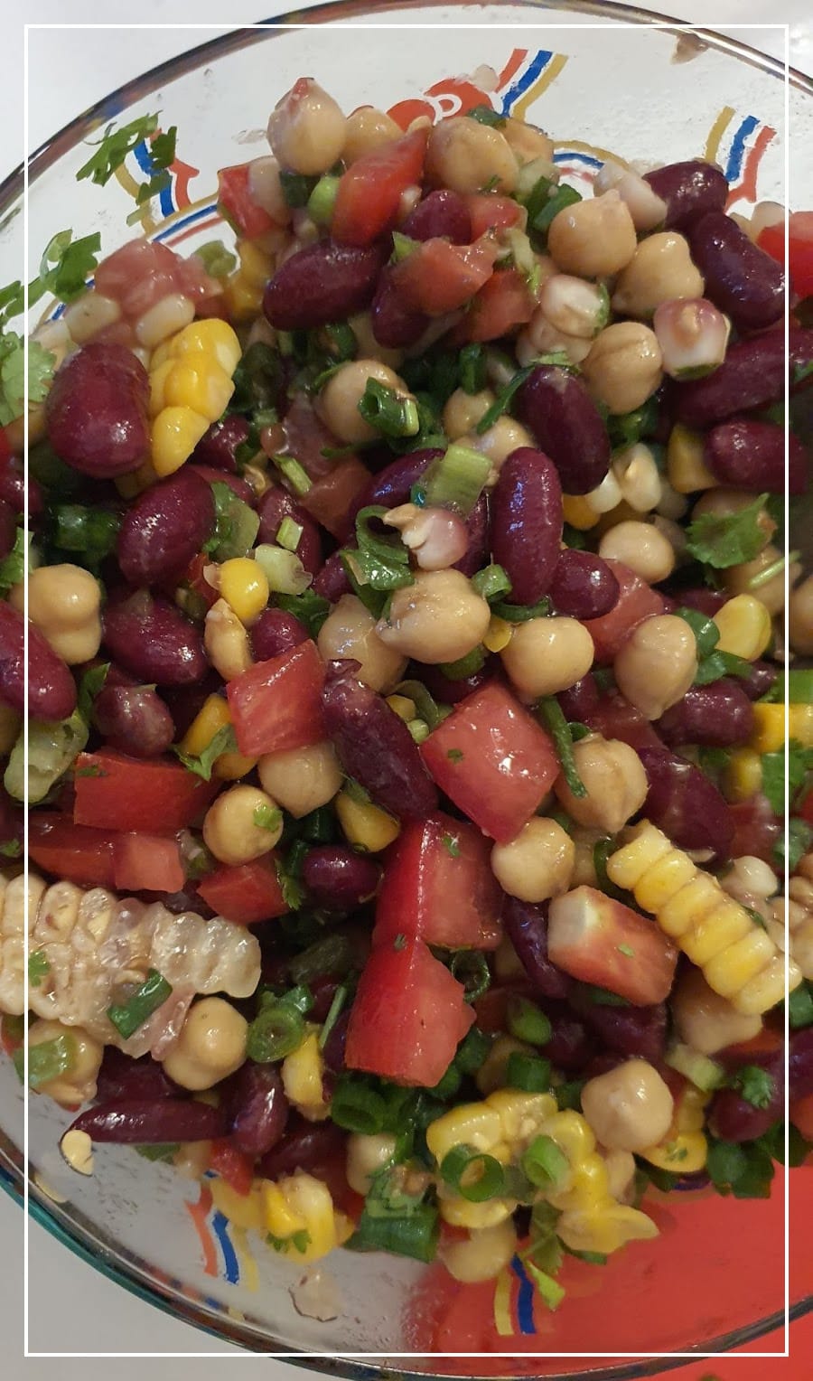 a top-down view into a large tupperware bowl full of bean salad; black beans, garbanzo beans, tomato, corn, scallions, and cilantro are all visible and coated in dressing.